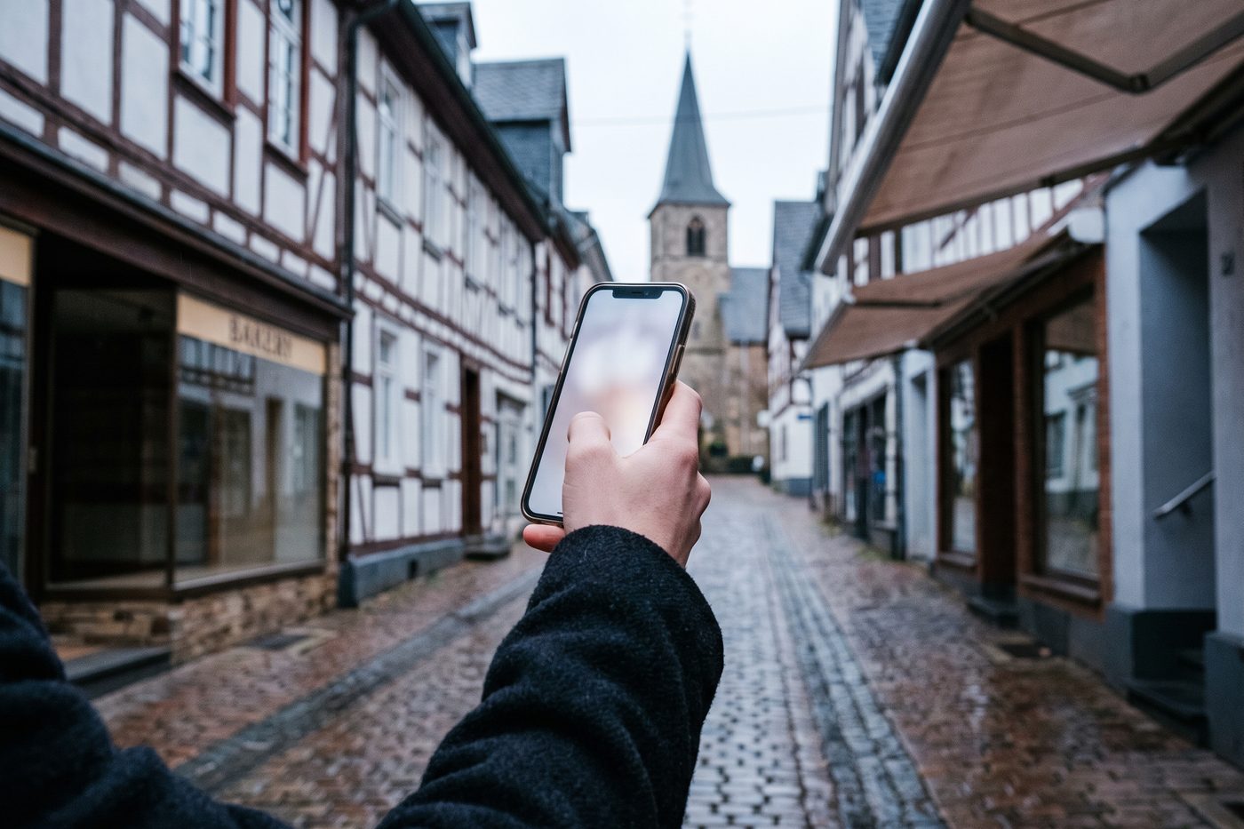 Hand hält ein Smartphone auf der Hauptstraße einer Kleinstadt im Westerwald